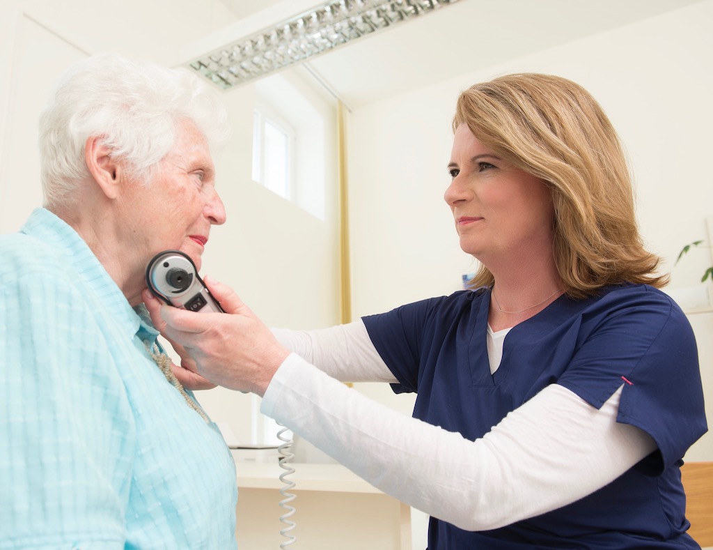 Ärztin untersucht ältere Patientin mit einem medizinischen Gerät am Hals.